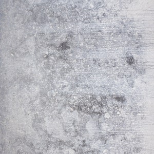 Op de afbeelding: Een close-up van een grijs betonnen oppervlak met een ruwe textuur en witte en zwarte vlekken.