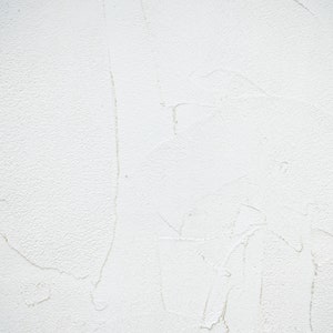 Op de afbeelding: Een witte, getextureerde muur met subtiele onvolkomenheden en vage lijnen.