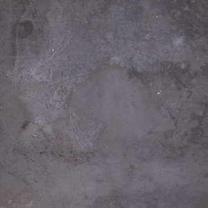 Op de afbeelding: Een close-up van een grijs betonnen oppervlak met een ruwe textuur. Het oppervlak heeft een paar kleine witte vlekken en enkele vage lijnen.