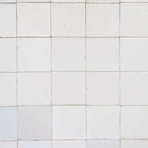 Pode incluir: Uma parede de azulejos brancos com um padrão de grade. Os azulejos são ligeiramente irregulares e têm um aspecto desgastado.
