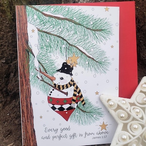 May include: A Christmas card featuring a snowman illustration. The snowman wears a black top hat, a striped scarf, and a red and green patterned body. The card includes the text "Every good and perfect gift is from above James 1:17."