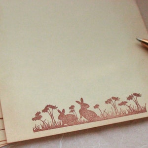 May include: A stack of blank stationery with a brown bunny rabbit silhouette design at the bottom. The design includes a line of grass and small flowers.