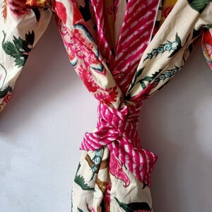 Pu&ograve; includere: Una vestaglia di cotone bianco con stampa floreale rosa e bianca. La vestaglia &egrave; legata in vita con una cintura rosa e bianca a righe.