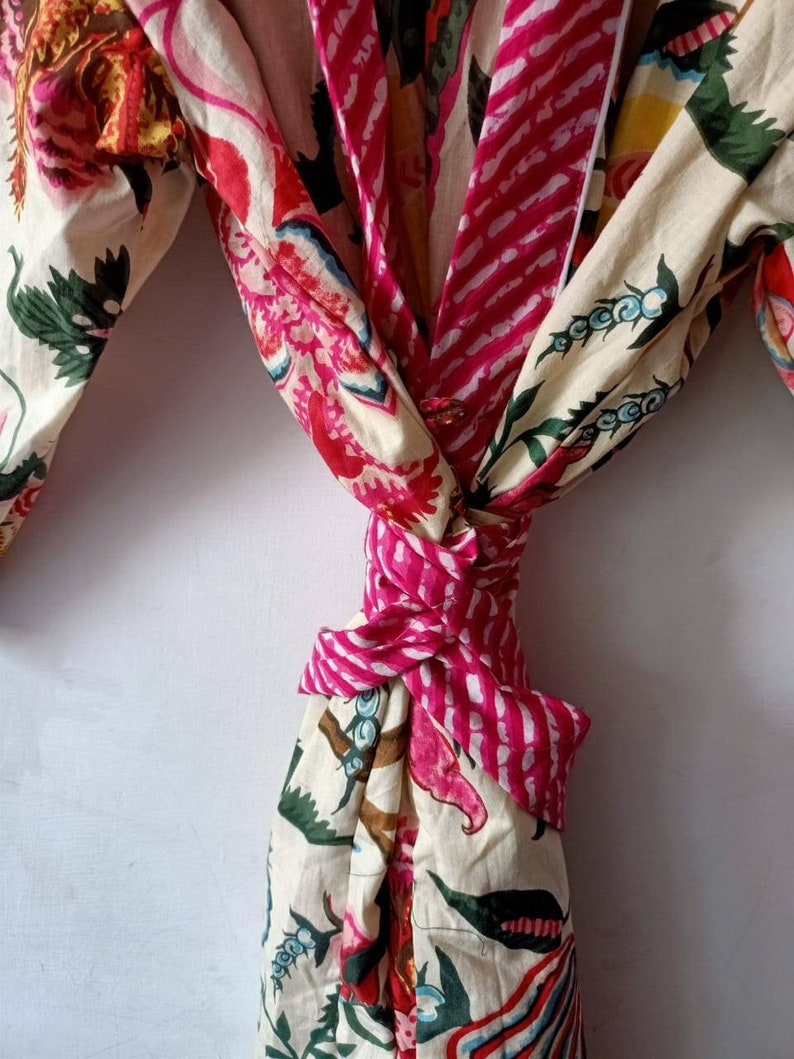 Pu&ograve; includere: Una vestaglia di cotone bianco con stampa floreale rosa e bianca. La vestaglia &egrave; legata in vita con una cintura rosa e bianca a righe.
