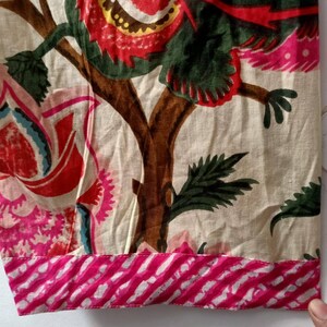 Pu&ograve; includere: Un tessuto color crema con una stampa floreale rosa e verde. Il tessuto ha un bordo a righe rosa e bianco.