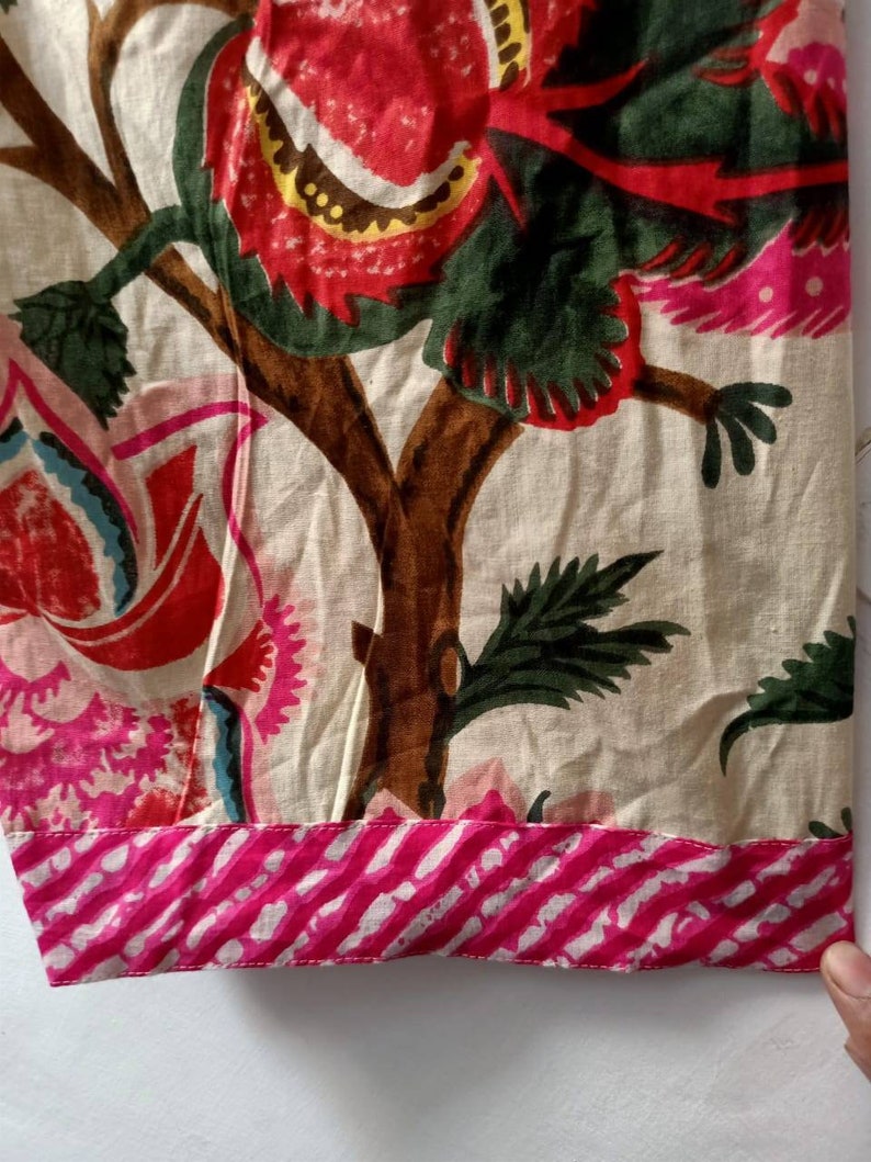 Pu&ograve; includere: Un tessuto color crema con una stampa floreale rosa e verde. Il tessuto ha un bordo a righe rosa e bianco.