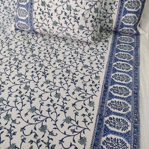 May include: White cotton bedding with a blue and green floral print. The bedding has a border with a repeating pattern of blue and green floral motifs.