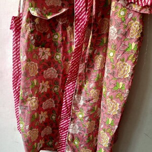 May include: A pink cotton robe with a floral print and a red and white striped tie. The robe has a white trim and two pockets.