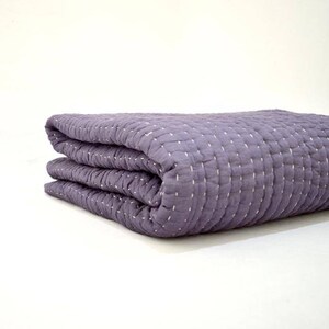 May include: A folded purple quilted throw blanket with white stitching.