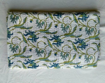 May include: A white kantha quilt with a floral pattern in shades of green and blue. The quilt is folded in half and is lying on a white surface.