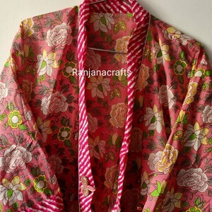 May include: A pink floral print cotton robe with a pink and white striped trim. The robe has a button closure and long sleeves. The text "Ranjanacrafts" is visible on the robe.