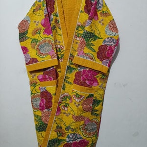 May include: A yellow floral print quilted robe with a long sleeve and a tie closure. The robe has a yellow trim and two pockets.