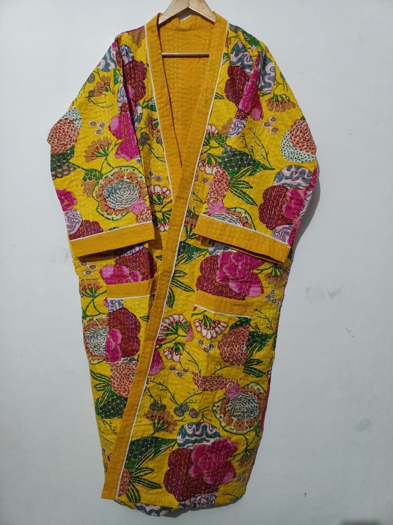May include: A yellow floral print quilted robe with a long sleeve and a tie closure. The robe has a yellow trim and two pockets.