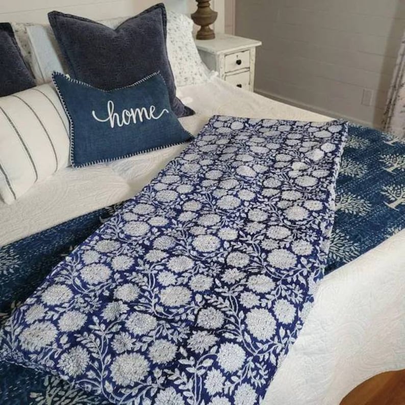 Pu&ograve; includere: Un trapunta con motivo floreale blu e bianco con sfondo bianco e fiori blu. La trapunta &egrave; piegata su un letto con cuscini blu e un cuscino con la parola "home" su di esso.
