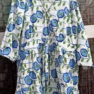 Puede incluir: Un vestido blanco de envolver con estampado floral azul. El vestido tiene un escote en V y un lazo en la cintura.