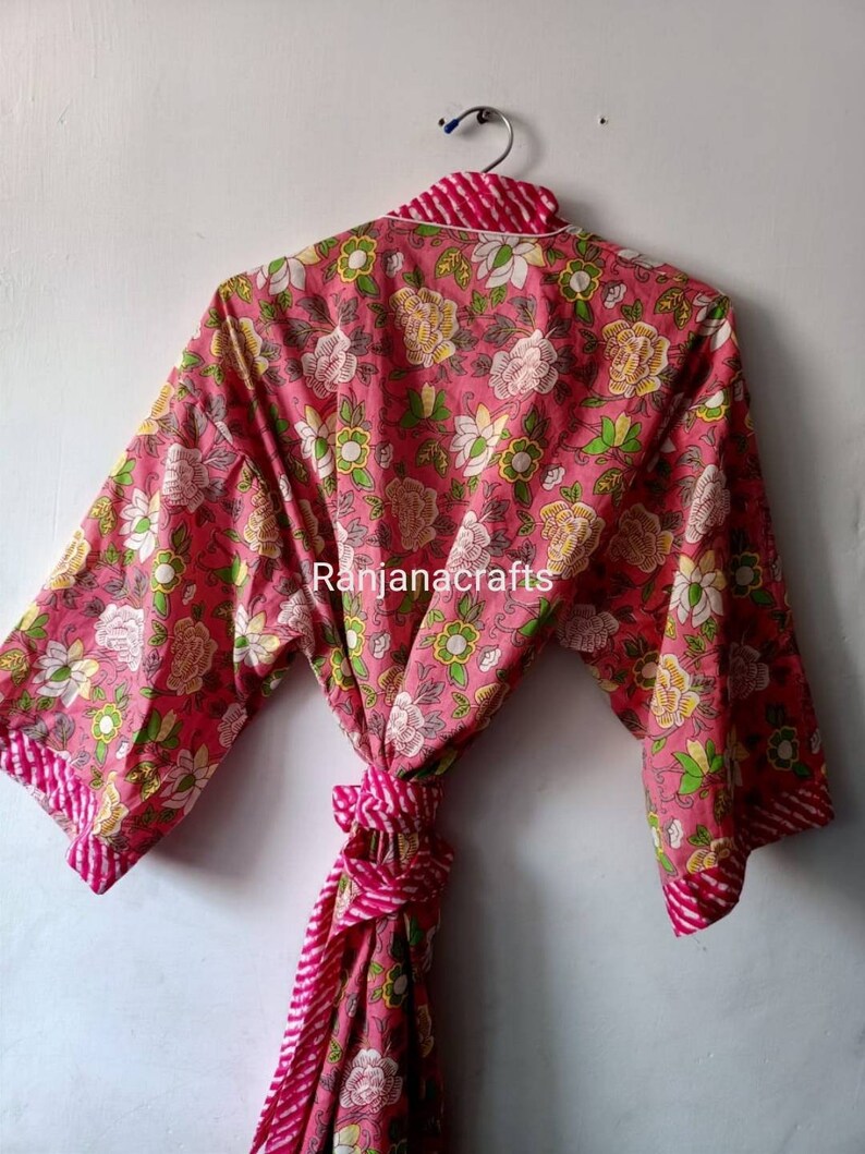 May include: A pink floral print cotton robe with a white trim and a pink and white striped tie. The robe has a traditional Japanese kimono style.