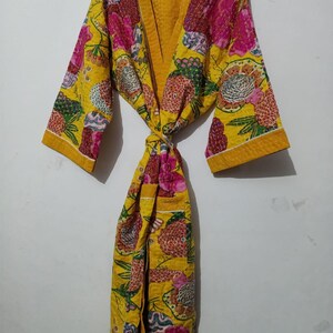 May include: A yellow quilted robe with a floral print in shades of pink, green, and blue. The robe has a tie belt and long sleeves.