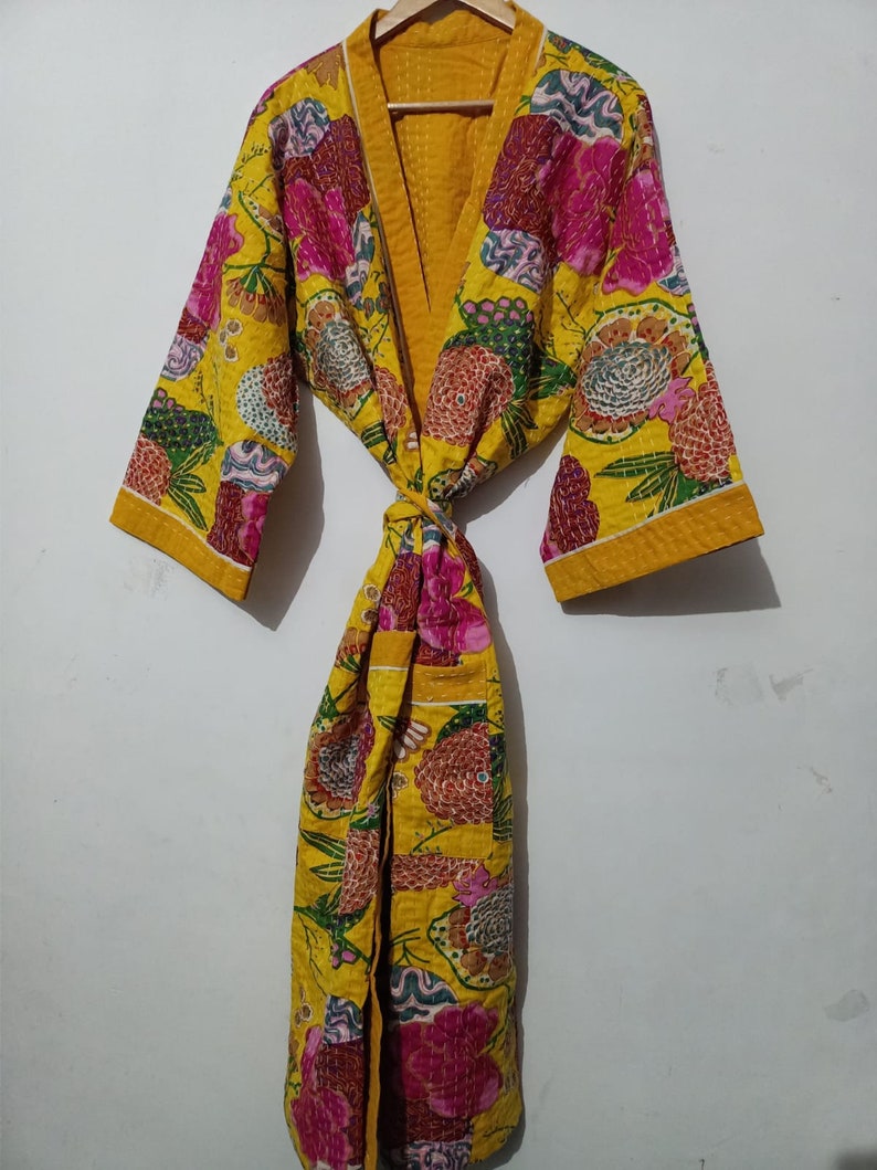 May include: A yellow quilted robe with a floral print in shades of pink, green, and blue. The robe has a tie belt and long sleeves.