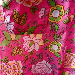 May include: Pink fabric with a floral pattern. The flowers are white, yellow, and green with pink outlines. The fabric has a textured surface.