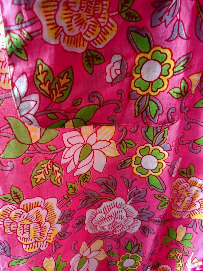 May include: Pink fabric with a floral pattern. The flowers are white, yellow, and green with pink outlines. The fabric has a textured surface.