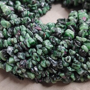Puede incluir: Una colección de pequeñas piedras preciosas pulidas que presentan una mezcla de verde vibrante, negro profundo e inclusiones ocasionales de color rosa magenta. Las piedras tienen formas irregulares, acabado liso y están dispuestas en racimo.