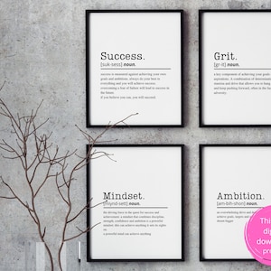 May include: Four black framed prints with white backgrounds and black text. The prints are titled "Success", "Grit", "Mindset", and "Ambition". Each print includes a definition of the word. The prints are hanging on a gray concrete wall.