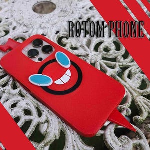 Puede incluir: Funda de teléfono roja con un diseño de cara de dibujos animados, con contorno negro, dientes blancos y ojos azules. La funda tiene una superficie texturizada y el texto "ROTOM PHONE" es visible. La funda tiene un diseño de rayo rojo.