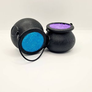 May include: Two black cauldron-shaped containers with handles. One cauldron has blue glitter inside and the other has purple glitter inside.