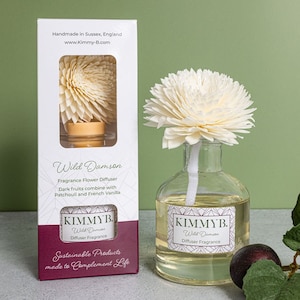 May include: A glass diffuser bottle with a wooden flower diffuser stick. The bottle is labelled "KIMMYB. Wild Damson Diffuser Fragrance". The diffuser is packaged in a white box with the text "Handmade in Sussex, England www.Kimmy-B.com Wild Damson Fragrance Flower Diffuser Dark fruits combine with Patchouli and French Vanilla. KIMMYB. Wild Damson Diffuser Fragrance Sustainable Products made to Complement Life."