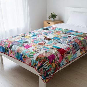 Könnte beinhalten: Ein farbenfroher Patchwork-Quilt mit einer Vielzahl von Blumen- und geometrischen Mustern. Der Quilt liegt auf einem weißen Bett, mit einem weißen Kissen und einem weißen Bettrahmen. Der Rand des Quilts ist mit roten Pompons verziert.
