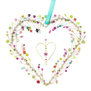 Può includere: Decorazione da parete a forma di cuore realizzata con filo argentato, adornata con perline colorate nei toni del rosa, verde, giallo e arancione. Un cuore dorato più piccolo è appeso al centro, con un nastro turchese per appenderlo.