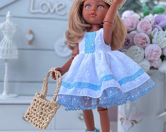 Könnte beinhalten: Eine Puppe mit langem braunem Haar trägt ein weißes Kleid mit blauer Blumenstickerei, einem blauen Bandbesatz und einem mehrlagigen Tüllrock. Die Puppe trägt einen beigen geflochtenen Hut, hellblaue und weiße Schuhe und eine kleine beige geflochtene Handtasche.
