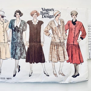 May include: A vintage sewing pattern for five different dresses. The pattern is for Vogue's Basic Design and is numbered 1611. The dresses are all knee-length and have a variety of styles, including a button-up dress, a dress with a bow, and a dress with a collar.