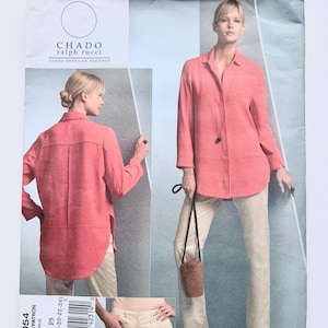 May include: A Vogue American Designer sewing pattern envelope for Chado Ralph Rucci design V1054. The front displays a coral-colored long-sleeved shirt with a collar and a curved hem, paired with beige trousers. Includes size range 16-24.