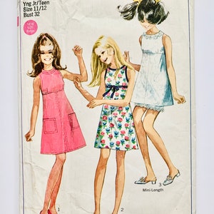 May include: A vintage Simplicity sewing pattern for a young junior or teen girl's dress. The pattern is for a mini-length dress with a variety of styles, including a pink dress with pockets, a floral print dress, and a white dress with lace trim. The pattern number is 7662 and the price is 65 pence.