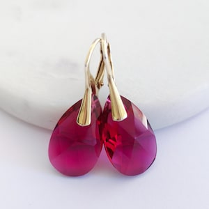 May include: A pair of gold dangle earrings with teardrop-shaped red crystal stones.