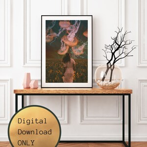 May include: A digital download print of a woman walking through a field of sunflowers with jellyfish floating above her. The background is a dark blue sky with clouds. The image is in a black frame and is on a wooden table.