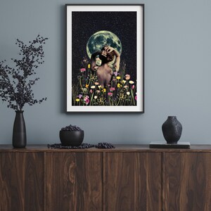 May include: A framed print of a woman standing in a field of flowers under a full moon. The woman is facing away from the viewer and has her arms raised above her head. The moon is a bright white and the sky is dark blue with stars.