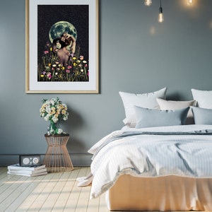 May include: A framed print of a woman standing in a field of flowers under a full moon. The woman is facing away from the viewer and has her hand on her head. The moon is a bright white and the sky is dark blue with stars. The flowers are a variety of colors, including pink, purple, yellow, and white.