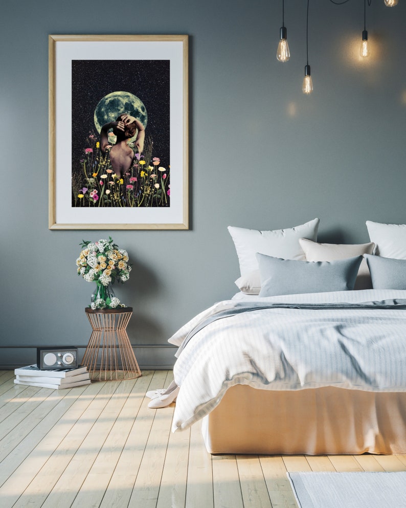 May include: A framed print of a woman standing in a field of flowers under a full moon. The woman is facing away from the viewer and has her hand on her head. The moon is a bright white and the sky is dark blue with stars. The flowers are a variety of colors, including pink, purple, yellow, and white.