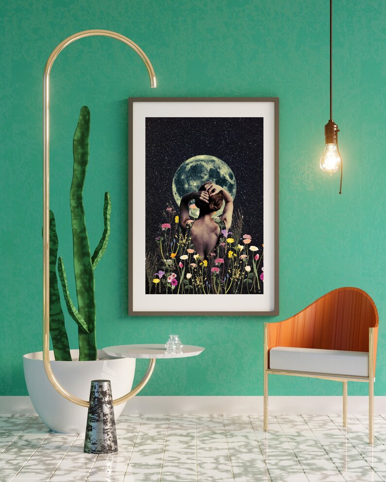 May include: A framed print of a woman standing in a field of flowers with a full moon in the background. The woman is facing away from the viewer and has her arms raised above her head. The print is set against a teal green wall with a cactus plant and a gold metal stand with a white round table top.
