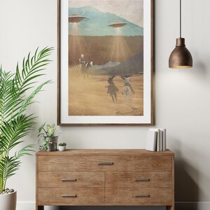 Puede incluir: Una impresi&oacute;n enmarcada de una ilustraci&oacute;n de estilo vintage que representa a vaqueros montando a caballo en un paisaje des&eacute;rtico con tres platillos voladores en el cielo arriba. La impresi&oacute;n tiene un aspecto desgastado y texturizado.