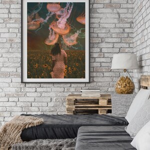 May include: A framed print of a woman in a field of sunflowers with jellyfish floating in the sky above her. The jellyfish are a pale orange color and have long tentacles.