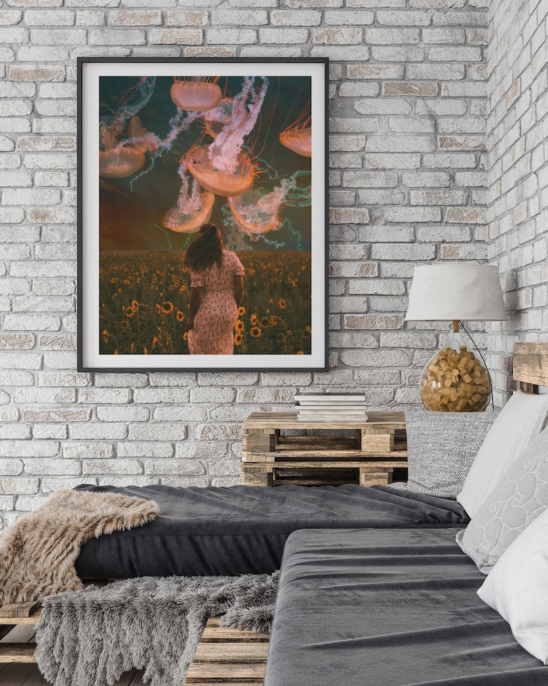 May include: A framed print of a woman in a field of sunflowers with jellyfish floating in the sky above her. The jellyfish are a pale orange color and have long tentacles.