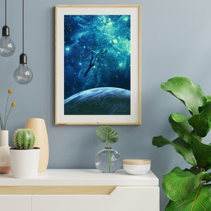 May include: A framed print of a blue and green galaxy with a silhouette of a plane flying over a planet. The frame is light wood and the print is on a white background.