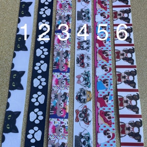 May include: Six different ribbon trims with various patterns. The first ribbon has a black cat design on a white background. The second ribbon has a white paw print design on a black background. The third ribbon has a colorful design with dogs wearing hats and sunglasses. The fourth ribbon has a white dog design with sunglasses on a white background. The fifth ribbon has a pink and blue design with dogs wearing hats and sunglasses. The sixth ribbon has a red and white design with dogs wearing sunglasses.