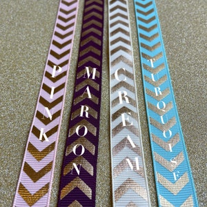 May include: Four ribbon spools with gold chevron patterns and the words "PINK", "MAROON", "CREAM", and "TURQUOISE" printed on them.