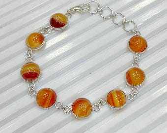 Pode incluir: Uma pulseira de prata com dez pedras redondas de ágata polida, laranja e vermelha. As pedras são engastadas em biséis individuais de prata e conectadas por pequenas elos de prata. Fecho de lagosta.
