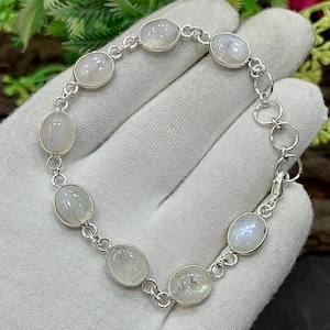 May include: A silver bracelet featuring oval, iridescent moonstone cabochons. The stones are set in individual bezels and linked together with a delicate chain. The bracelet is approximately 7 inches long.