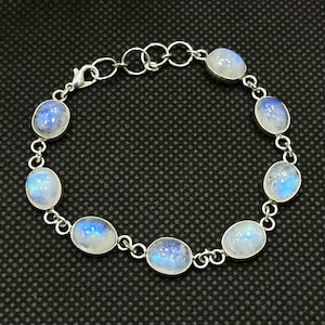 Pode incluir: Uma pulseira de corrente de metal prateado com oito pedras da lua ovais e translúcidas com um brilho azul iridescente. A pulseira inclui um fecho lagosta e uma série de anéis circulares para um ajuste de tamanho regulável.